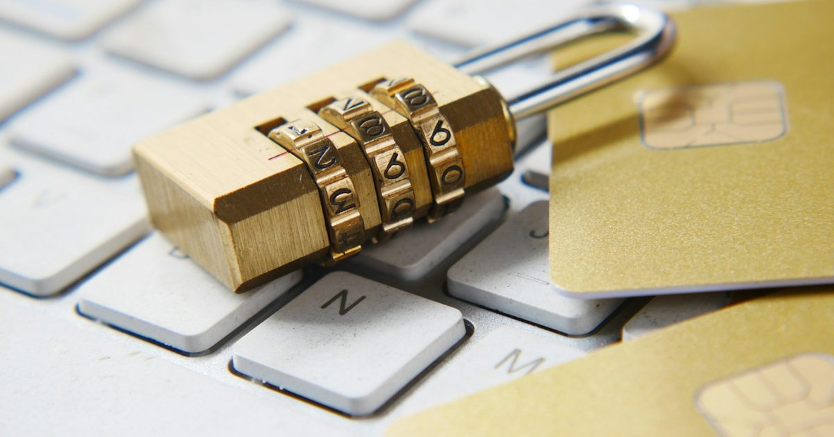 A brass combination padlock resting on a laptop keyboard next to gold chip cards